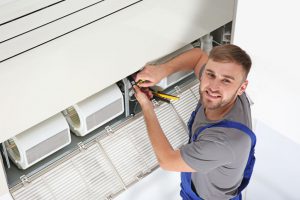 Young male technician repairing air conditioner indoors